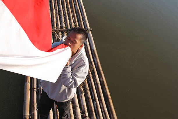 Man On Bamboo Raft Respectfully Kisses The Indonesian Flag, Showing Patriotism And Love For His Country