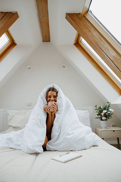 istock Happy woman is sitting on a bed wrapped in a white blanket 2226893076