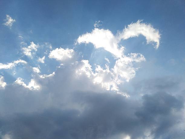 The image shows a serene blue sky with white clouds, partially illuminated by sunlight. The gentle contrast between light and shadow creates a calm and uplifting atmosphere, perfect for conveying tranquility and natural beauty.