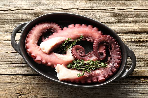 istock Fresh raw octopus and thyme in baking dish on wooden table, top view 2226911056