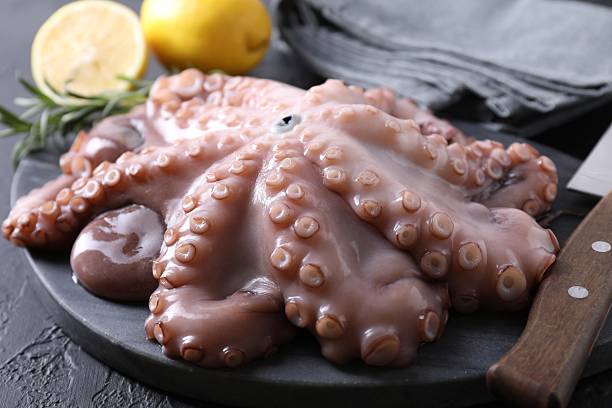 istock Fresh raw octopus, lemon, rosemary and knife on black table, closeup 2226911057