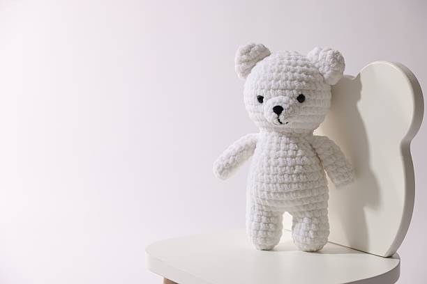 Cute crocheted bear on wooden chair against white background, space for text