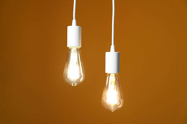 istock Light bulbs hanging on cords against orange background 2226911790