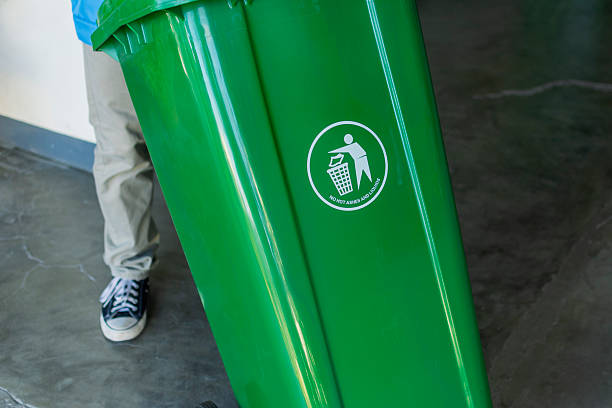 istock An anonymous person is pictured pushing a large green garbage bin, aligning with the weekly trash disposal routine. 2226912035