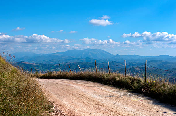 fence along a white country road against the sky with clouds