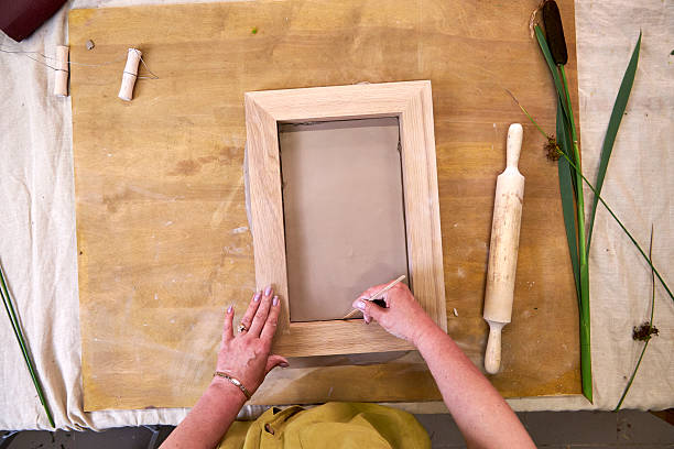 istock Placing and smoothing clay inside wooden frame to prepare base for plaster relief. Hands using sculpting tool to align edges during DIY floral artwork creation in step-by-step tutorial 2226917424