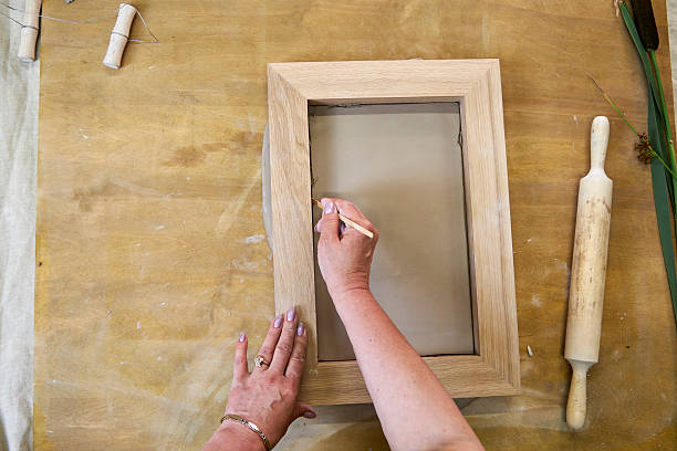 istock Placing and smoothing clay inside wooden frame to prepare base for plaster relief. Hands using sculpting tool to align edges during DIY floral artwork creation in step-by-step tutorial 2226917437