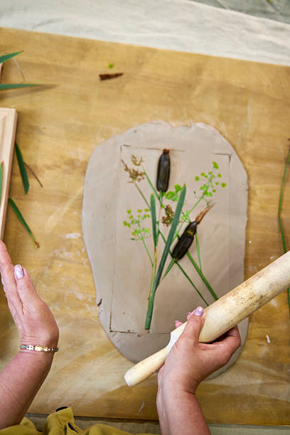 istock Pressing flowers and leaves into clay with a rolling pin to create botanical imprint for plaster relief. Hands flattening plants in DIY step-by-step tutorial for handmade floral art project 2226918242