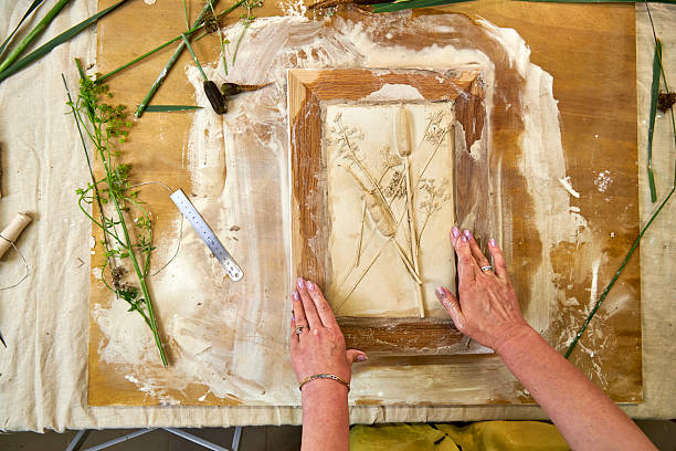istock Hands holding finished botanical plaster relief in a wooden frame. DIY floral artwork with imprints of flowers and leaves, final step of handmade decorative craft project in creative workshop 2226921433
