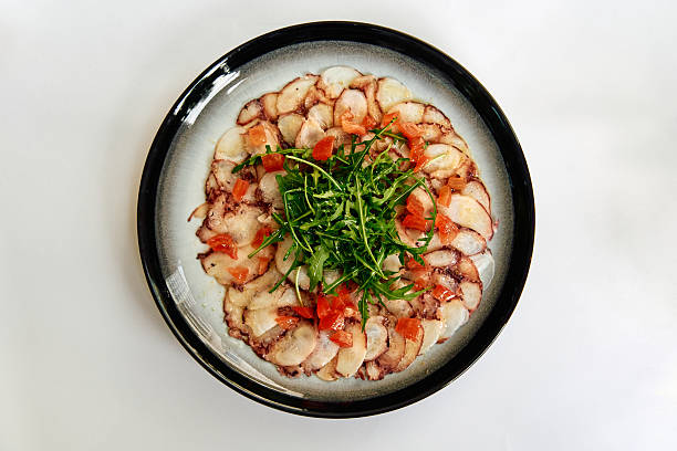 Savory Octopus Carpaccio Served on a Elegant Plate with Fresh Greens and Diced Tomatoes Garnish for a Delightful Culinary Experience