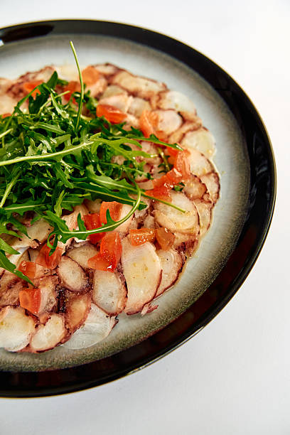 istock A beautifully arranged plate featuring thinly sliced octopus with fresh tomatoes and arugula, highlighting vibrant colors and exquisite culinary presentation. 2226924372