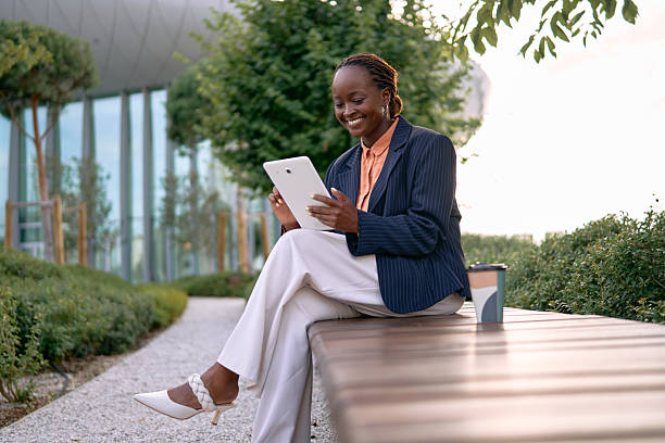 istock Smiling businesswoman using digital tablet while sitting on bench in city park 2226928969