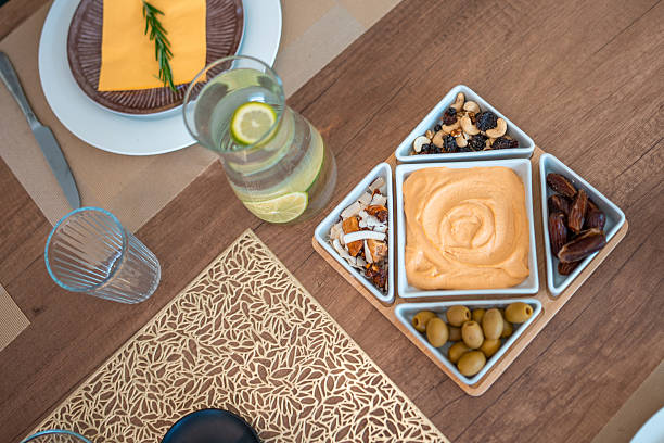 A sophisticated dinner table setup with a decorative appetizer platter featuring olives, nuts, dried fruits, and hummus, paired with refreshing lemon water on a wooden surface. The scene exudes warmth and elegance.