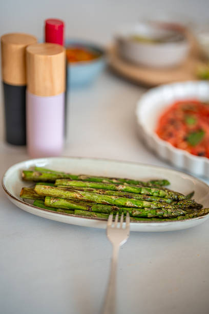 A plate of grilled asparagus on a white ceramic dish set on a kitchen counter, surrounded by colorful dinner party preparations and modern tableware.