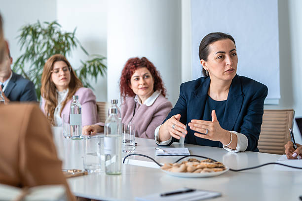 A diverse group of business executives, including men and women, engage in a strategy meeting in a modern boardroom. Natural lighting, professional attire, and collaborative gestures enhance the professional and inclusive atmosphere.