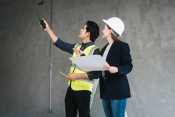 istock Asian male and female engineers wearing safety vests and helmets inspect structural elements, review blueprints, plan material choices bricks, steel, concrete during home renovation project on-site. 2226938489