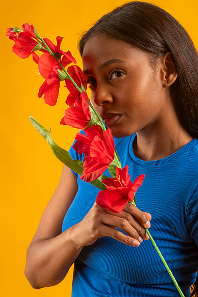 Young woman smelling red gladiolus flowers on a yellow background, creating a vibrant and colorful portrait