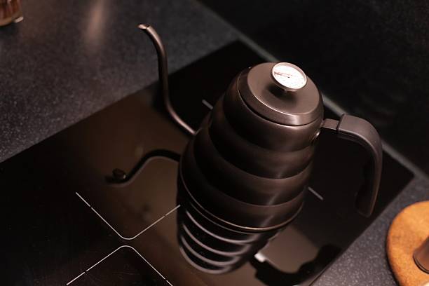 istock A matte black gooseneck kettle with a built-in thermometer is placed on a sleek black stovetop. Its curved spout and ergonomic handle are ideal for precise pouring in coffee or tea brewing. 2226950030