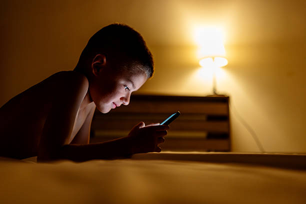 istock Young Boy Using a Smartphone While Lying in a Dimly Lit Bedroom 2226950777