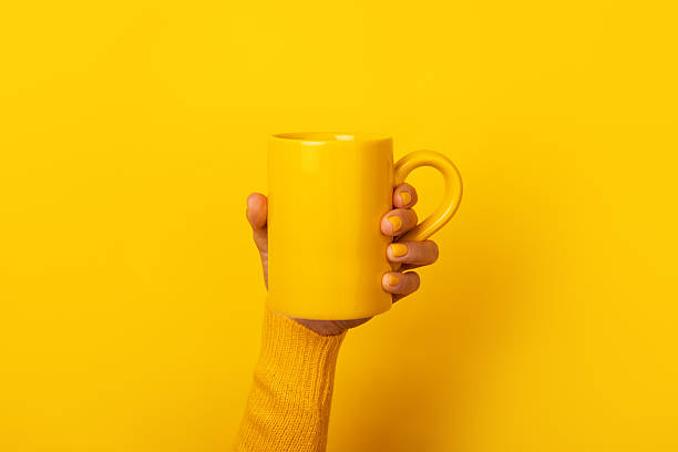 istock Hand with yellow nails and sweater holding a plain yellow ceramic mug in front of a solid yellow background. 2226951768