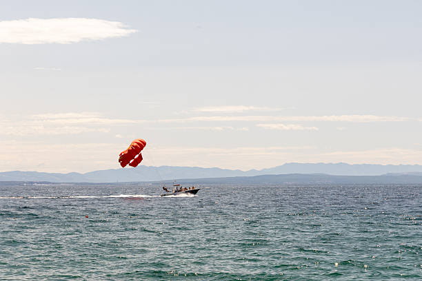 Colorful parachute is lifted by a speedboat over the ocean, showcasing a thrilling summer activity with clear skies and distant mountains in view