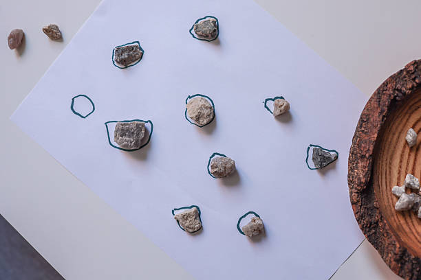 Educational activity with natural stones placed on outlined shapes on white paper. Creative matching game for children to develop observation, focus, and fine motor skills