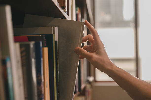 istock Hand picking a book or takes out from the shelf, pulling book from bookshelf in public library in university, college or high school in Education and literature concept 2226963607