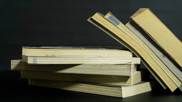 istock Stacked books with one tilted and falling beside the pile on dark background, storytelling concept of imbalance, reading habits, or everyday clutter 2226963612
