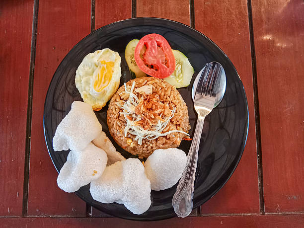 Nasi Goreng, Indonesian fried rice. Fried rice with chicken and egg garnished with fresh cucumber, tomato slices and crackers. Indonesian food.