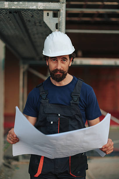 istock Construction worker reading blueprints on site wearing hardhat and overalls 2226964106