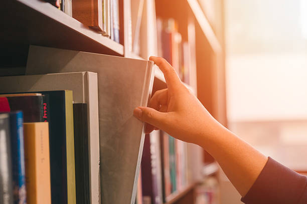 istock Hand picking a book or takes out from the shelf, pulling book from bookshelf in public library in university, college or high school in Education and literature concept 2226964316