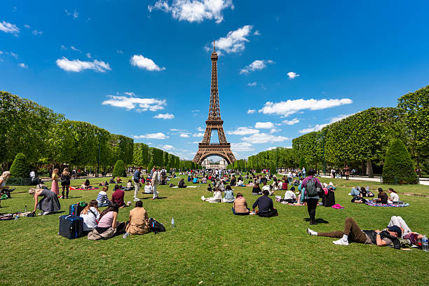 Paris, France - May 23, 2025: Eiffel Tower seen from Champ de Mars park with green lawn and visitors under sunny sky
