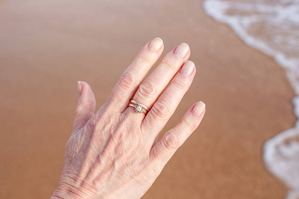 Woman's hand with wedding ring on sandy beach background. Seaside vacation, honeymoon.