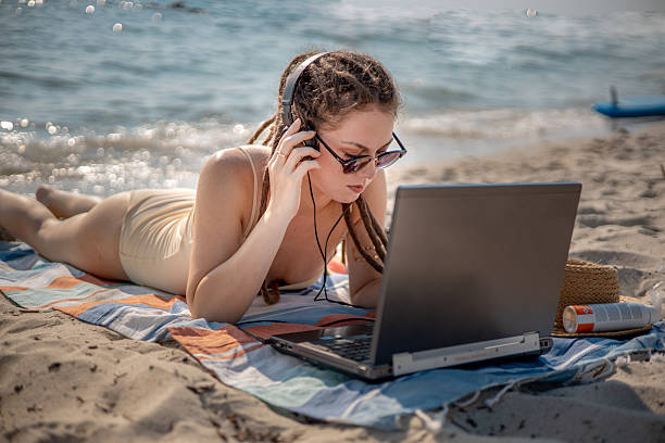 istock A dedicated virtual assistant comfortably working on her laptop while lying on a beach towel by the ocean - the freedom of remote summer work 2226999085