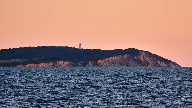 Evening view of the steep chalk cliffs and lighthouse on Hiddensee island near Rugen, Germany, with orange sky above the calm Baltic Sea during a serene summer sunset.