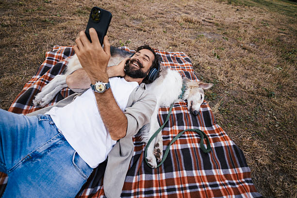 istock A man is lying or sitting on a checkered picnic blanket in a peaceful outdoor setting, using his smartphone while relaxing with his Borzoi dog 2227007111