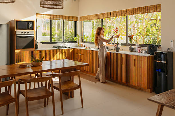 Mid-adult woman is arranging flowers in a vase in a modern wooden kitchen.