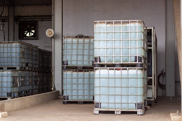 This photograph captures a warehouse setting where multiple containers filled with a translucent liquid are stored. The containers, each enclosed in a metallic framework, are stacked on pallets