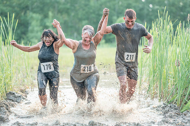 Three people energetically running through a muddy water obstacle course, showcasing teamwork and perseverance.