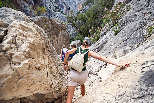 Group of hikers carefully maneuvering across massive limestone boulders on the floor of Su Gorropu Gorge, located in Sardinia’s Supramonte region. The scene unfolds in the gorge's labyrinth of colossal rocks shaped by millennia of erosion from the Rio Flumineddu. The hikers walk, balance and squeeze through narrow gaps between the boulders. The towering canyon walls rise dramatically on either side. The terrain is unforgiving, requiring agility, strength, and constant attention to footing.Shot with Canon R5.