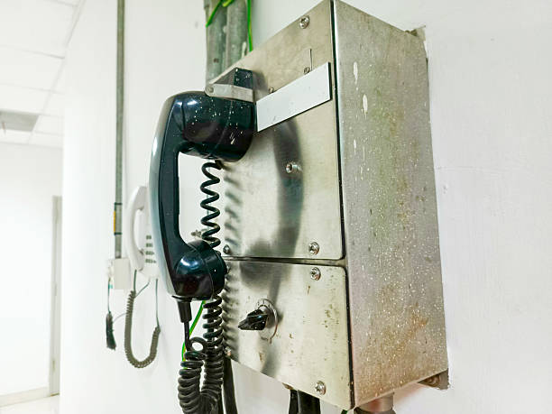 This image showcases an emergency communication system featuring a wall-mounted telephone, set against a clean, white wall. The industrial design of the metal box and the retro telephone