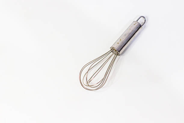 Asian hand holding a stainless steel balloon whisk in front of a pink background. The pose suggests kitchen preparation, baking, or cooking, ideal for culinary and food-related design themes.