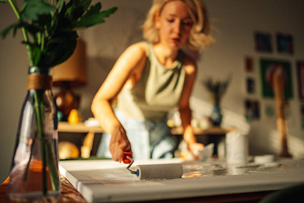 istock Woman artist priming canvas with paint roller in art studio 2227019697