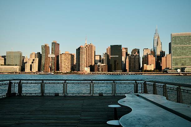 A wide pier with a metal table looks out toward the Chrysler Building and Midtown’s distinctive curved towers across the river.