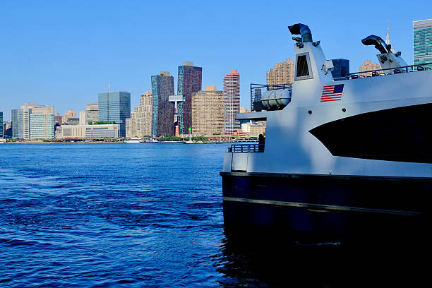 A New York City ferry glides across the East River toward Midtown’s gleaming towers on a sunny morning.