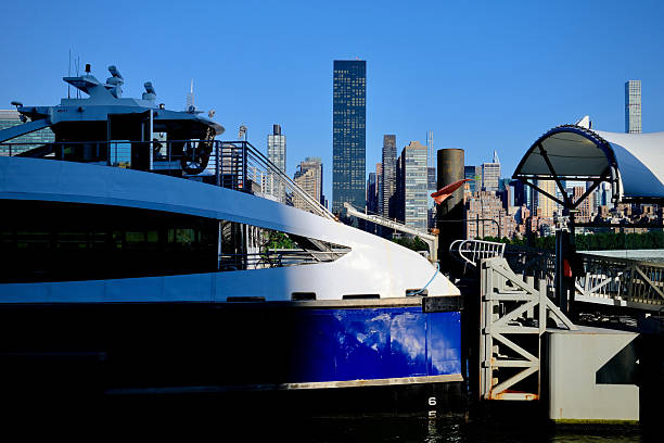 An NYC ferry is docked on the East River with the Midtown Manhattan skyline rising directly behind it under morning light.