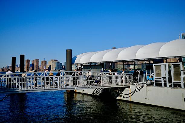Queens, New York, USA- July 21, 2025: Pedestrians walk through a curved canopy toward the NYC ferry dock at sunrise near Long Island City.