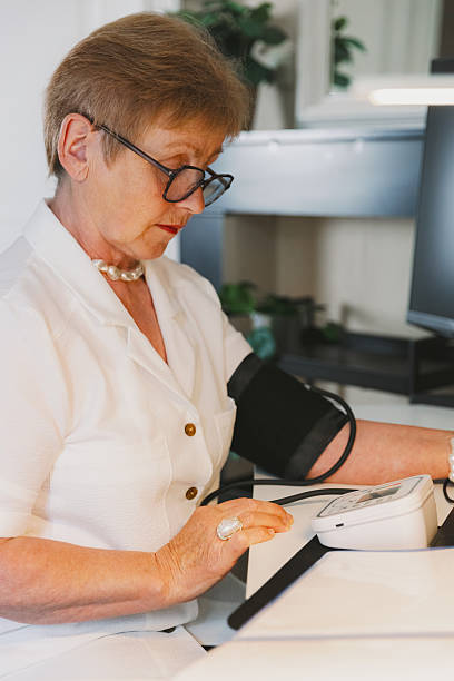 istock An elderly woman measures her blood pressure while working in her home office. 2227027224