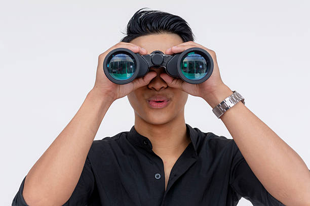 istock A young handsome guy looking impressed at something seen from his binoculars. Looking amazed. Wearing black polo shirt, isolated on a white background. 2227034624
