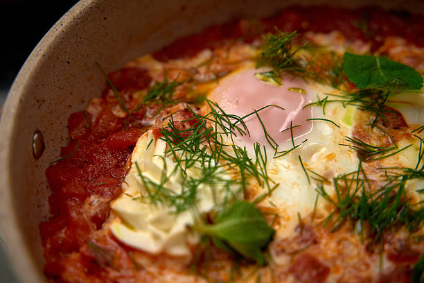 A Close-Up of a Delicious and Flavorful Dish Featuring Eggs Baked in a Rich Tomato Sauce Topped with Fresh Herbs and Creamy Ingredients